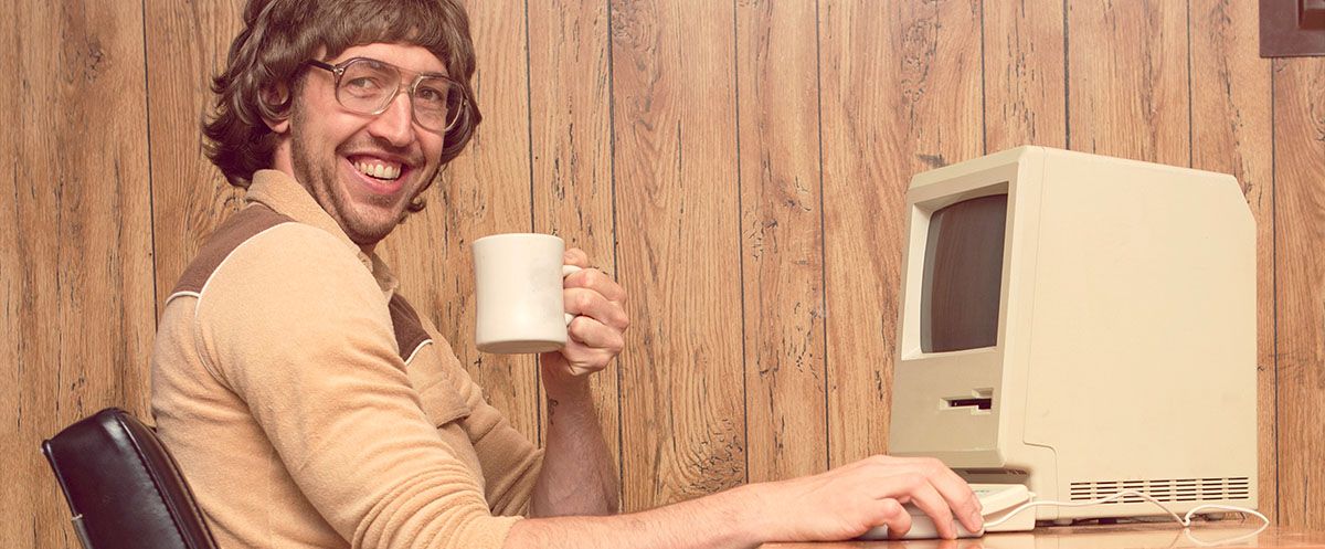 Bild på en man som håller i en mugg framför en gammal dator.